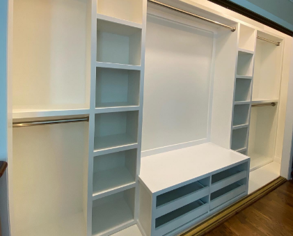 Spacious custom white closet with multiple hanging rods, shelving units, and a built-in bench for optimized storage.