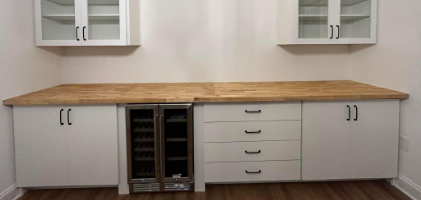 Modern white storage cabinet with drawers, glass-front upper cabinets, and a wooden countertop, featuring a built-in mini-fridge.